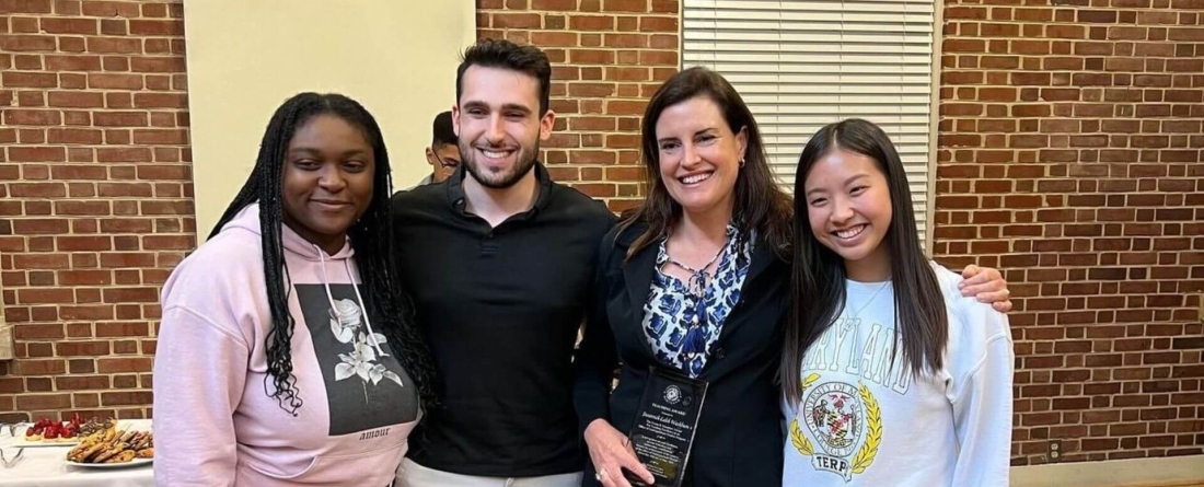 Susannah Washburn holds award standing with others against brick wall backdrop